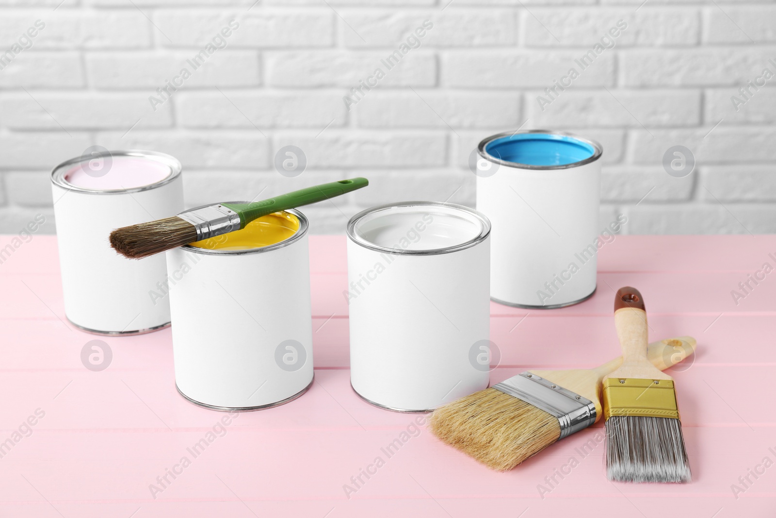 Photo of Cans of colorful paints and brushes on pink wooden table