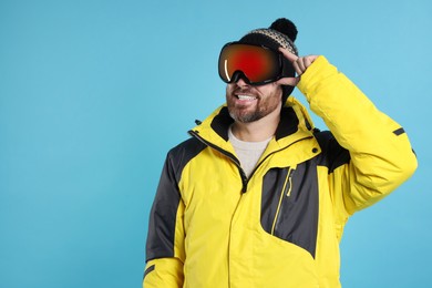 Winter sports. Happy man in ski suit and goggles on light blue background, space for text