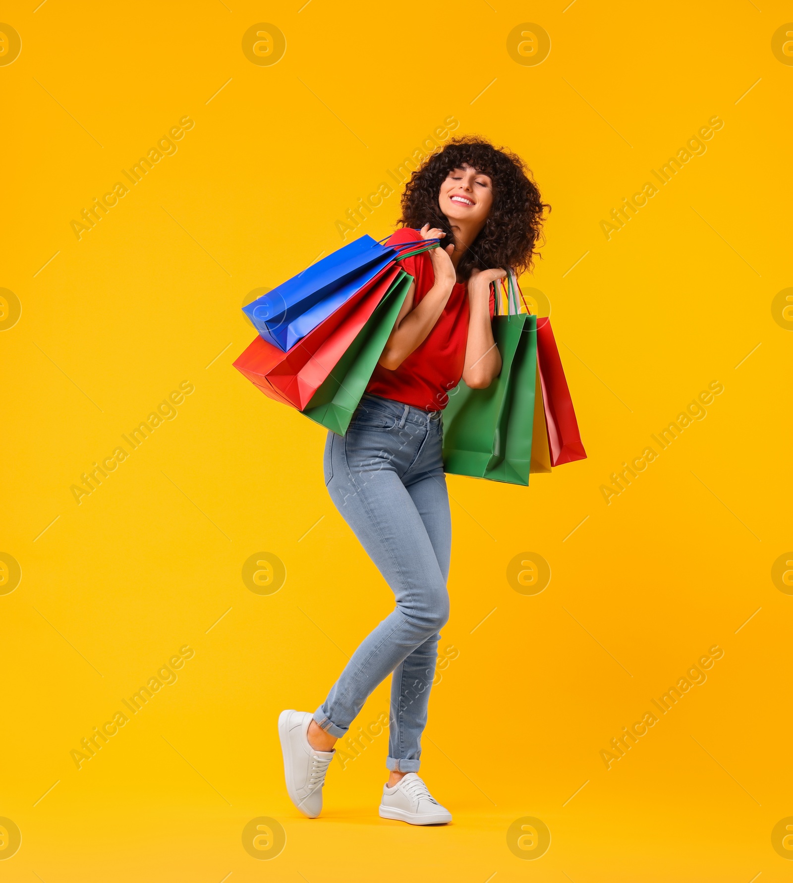 Photo of Happy young woman with shopping bags on yellow background