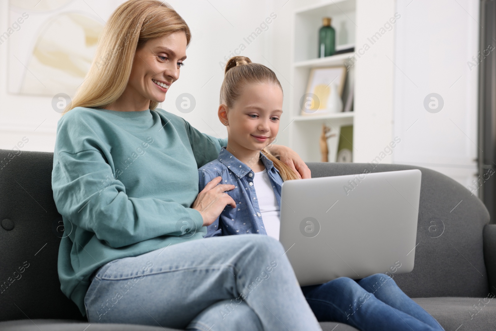 Photo of Happy woman and her daughter with laptop on sofa at home