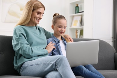 Happy woman and her daughter with laptop on sofa at home