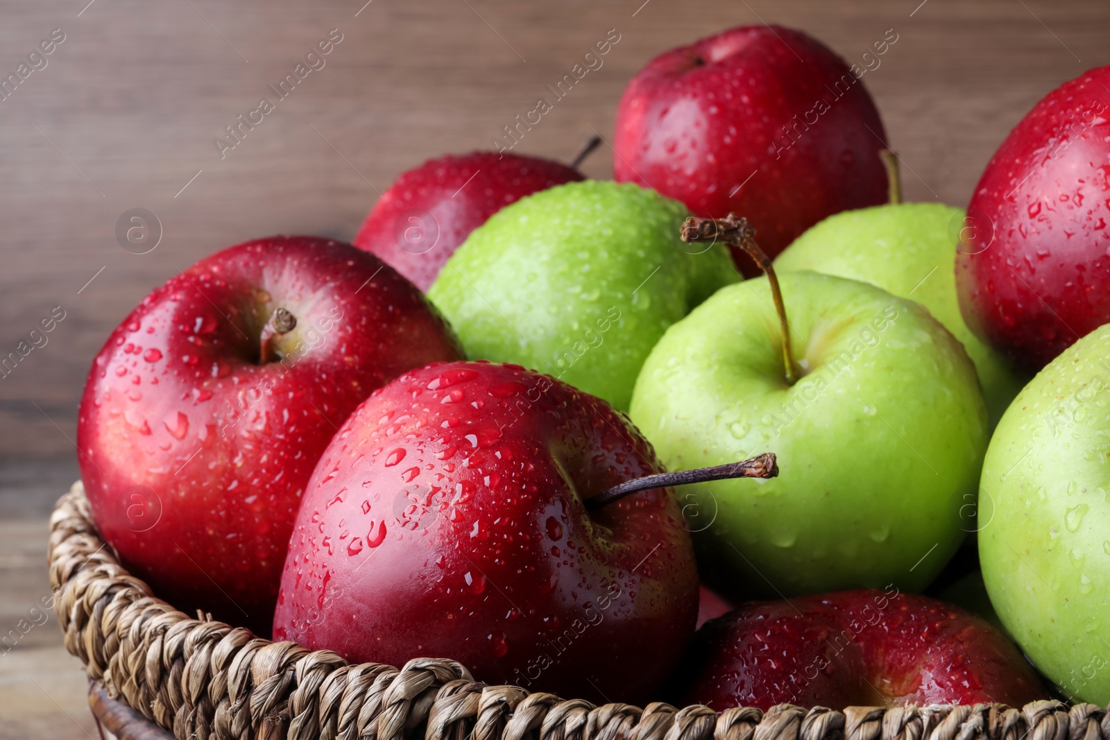 Photo of Fresh ripe green and red apples with water drops in wicker bowl, closeup