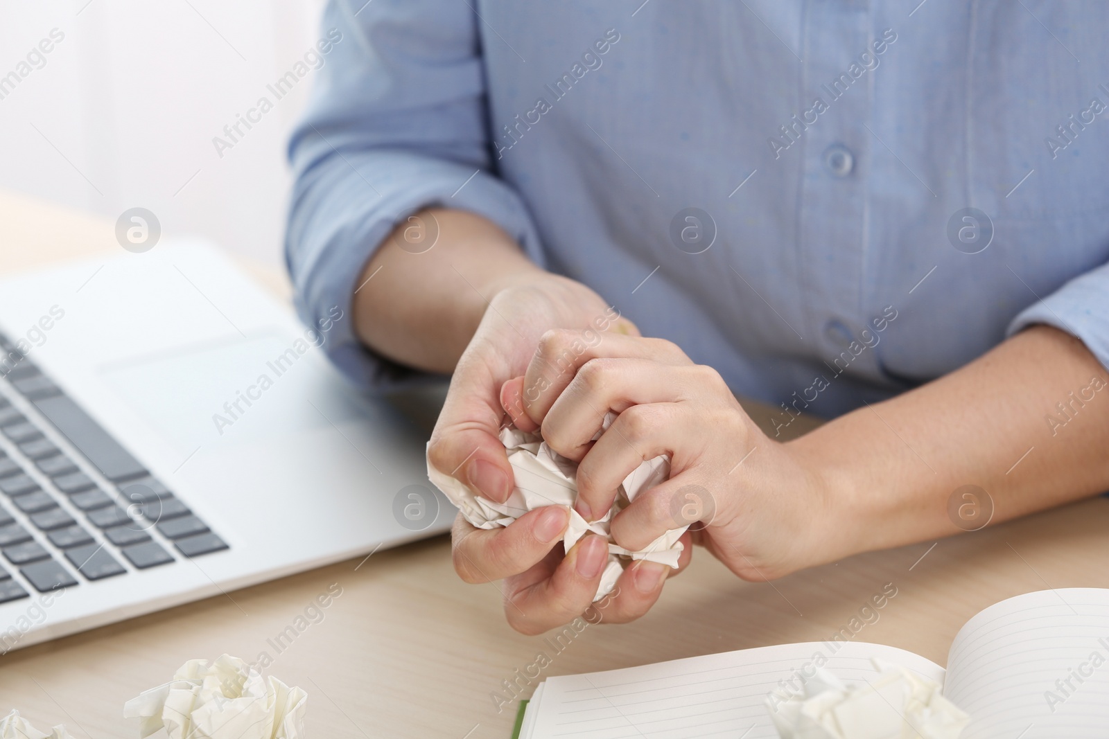 Photo of Woman crumpling paper at table, closeup. Generating idea