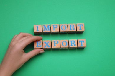 Photo of Woman making words Import and Export with wooden cubes on green background, top view