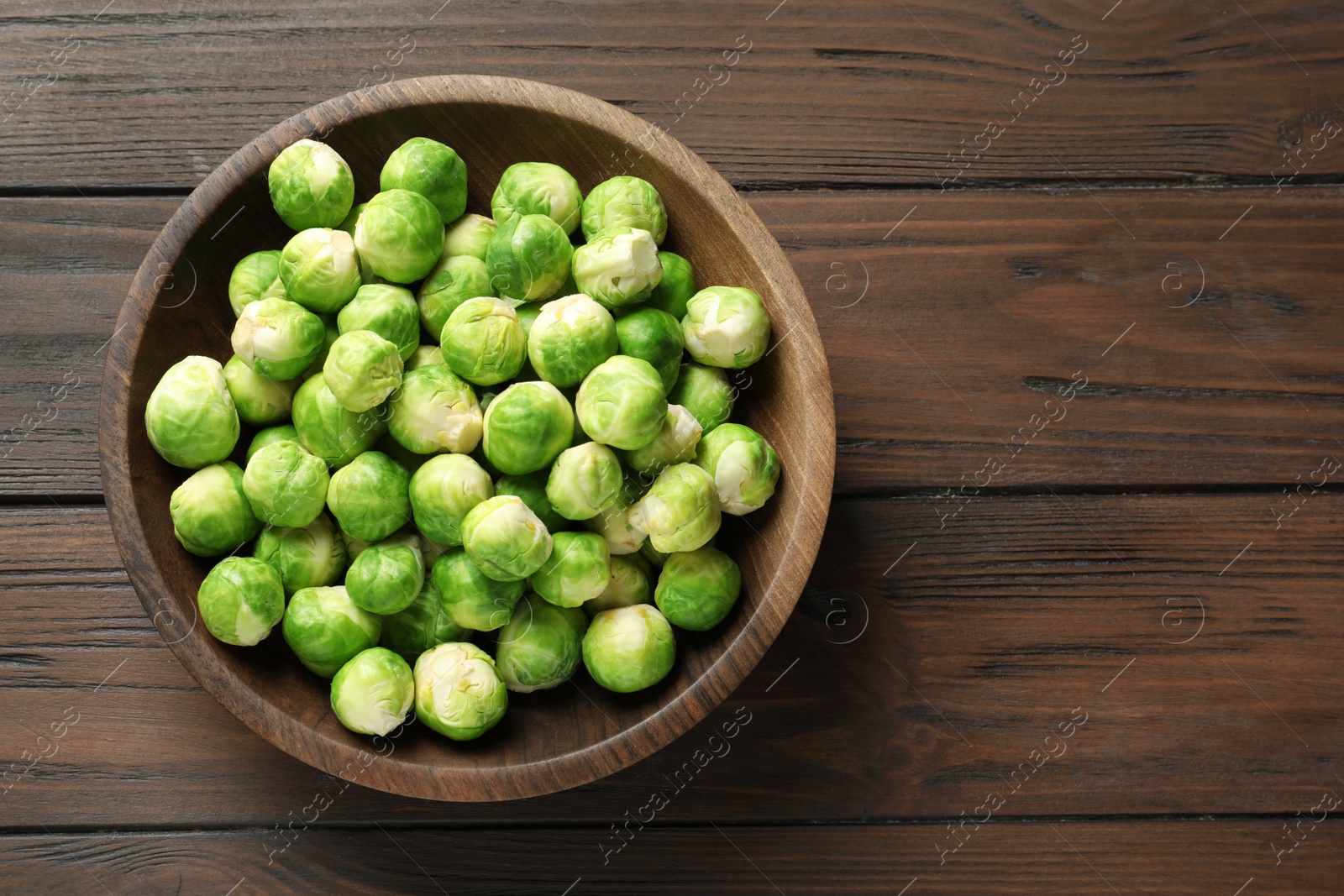 Photo of Bowl of fresh Brussels sprouts on wooden background, top view with space for text