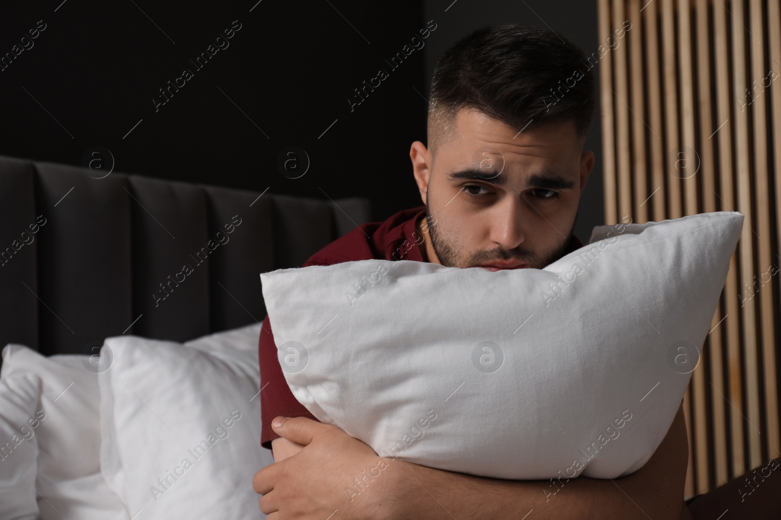 Photo of Sad man hugging pillow on bed at home. Space for text