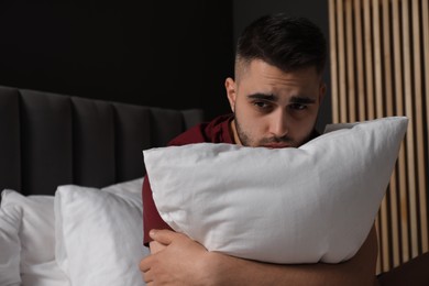 Photo of Sad man hugging pillow on bed at home. Space for text