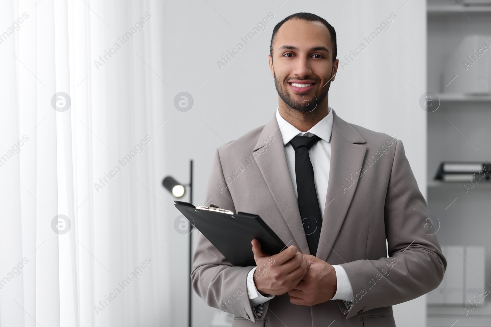 Photo of Portrait of smiling young man with clipboard in office, space for text. Lawyer, businessman, accountant or manager