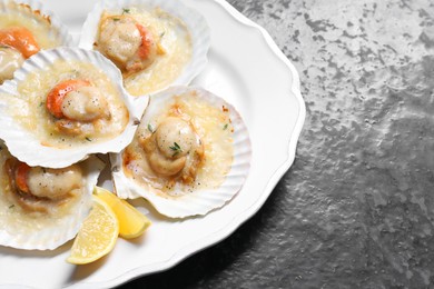 Fried scallops in shells and lemon on black textured table, closeup. Space for text