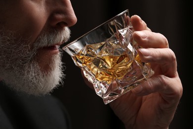 Photo of Senior man drinking whiskey from glass on black background, closeup