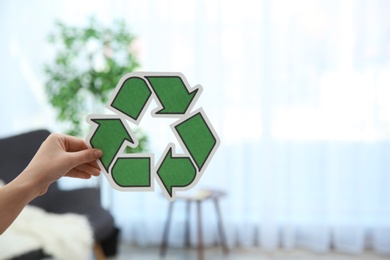 Woman holding recycling symbol on blurred background, closeup. Space for text