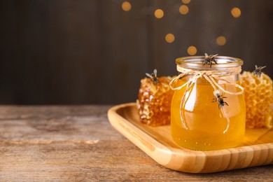 Image of Tasty aromatic honey and bees on wooden table, space for text