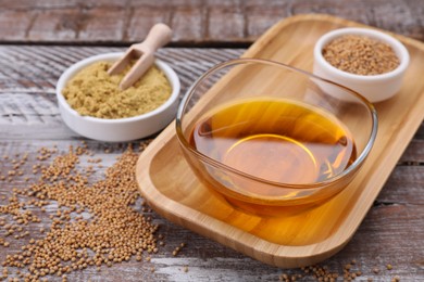 Photo of Bowl of natural oil, mustard seeds and powder on wooden table, closeup
