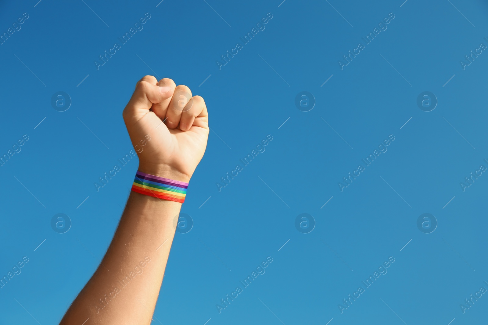 Photo of Man wearing gay wristband on hand against blue sky, closeup. Space for text