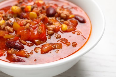 Bowl with tasty chili con carne on white wooden table, closeup