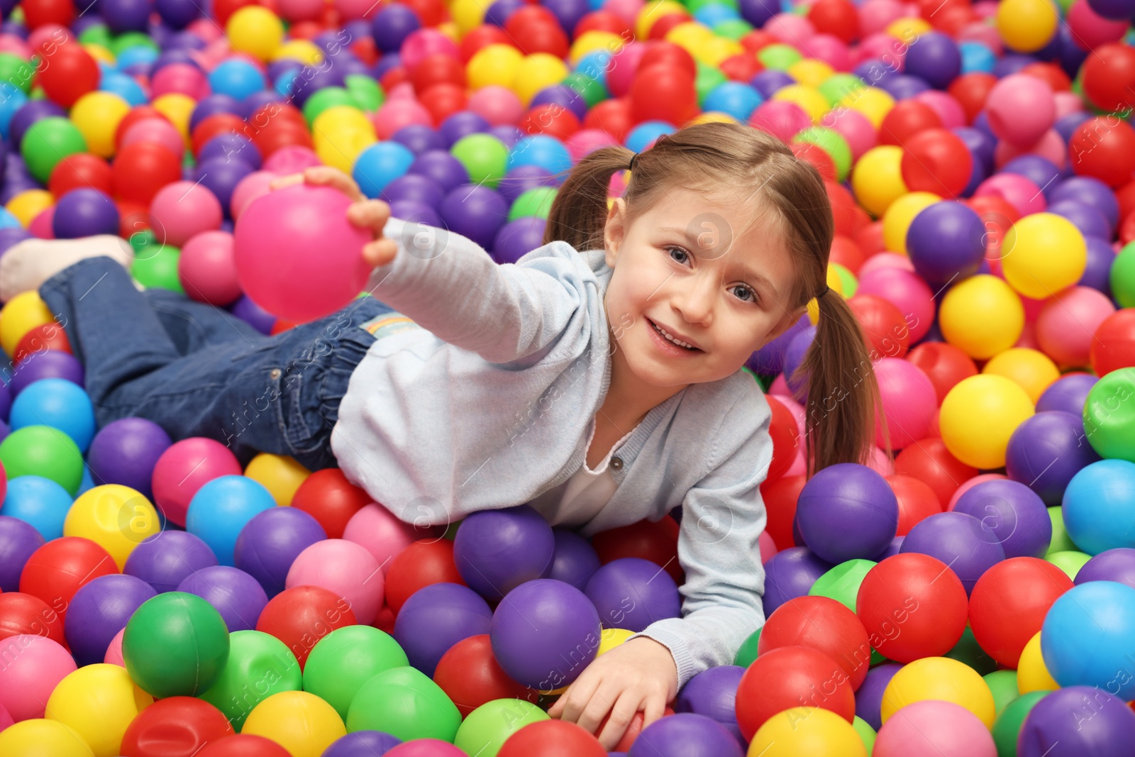 Photo of Happy little girl lying on many colorful balls in ball pit