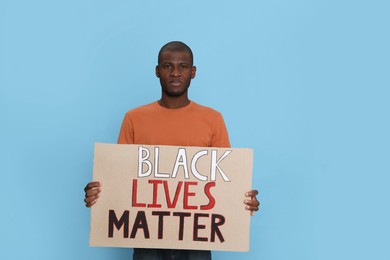 African American man holding sign with phrase Black Lives Matter on light blue background. Racism concept