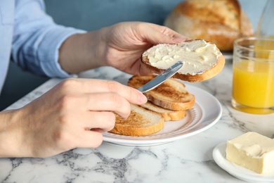 Woman spreading butter onto slice of bread over marble table, closeup