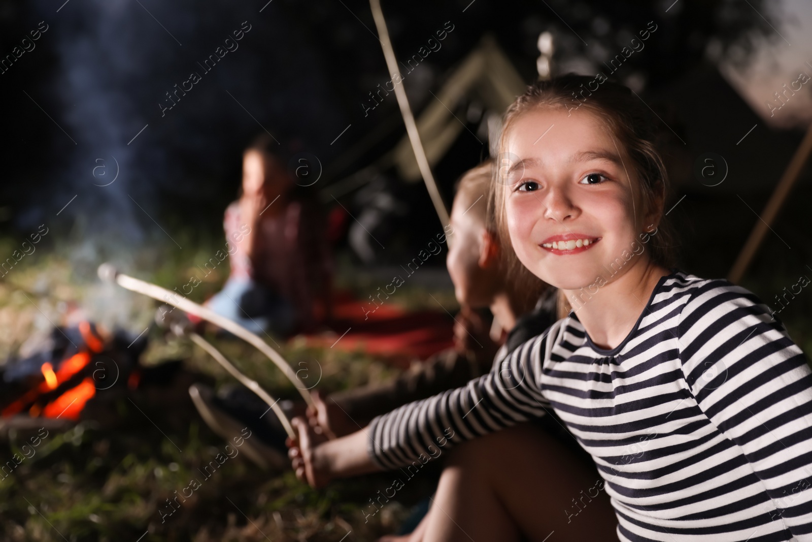 Photo of Adorable little girl near bonfire at night. Summer camp