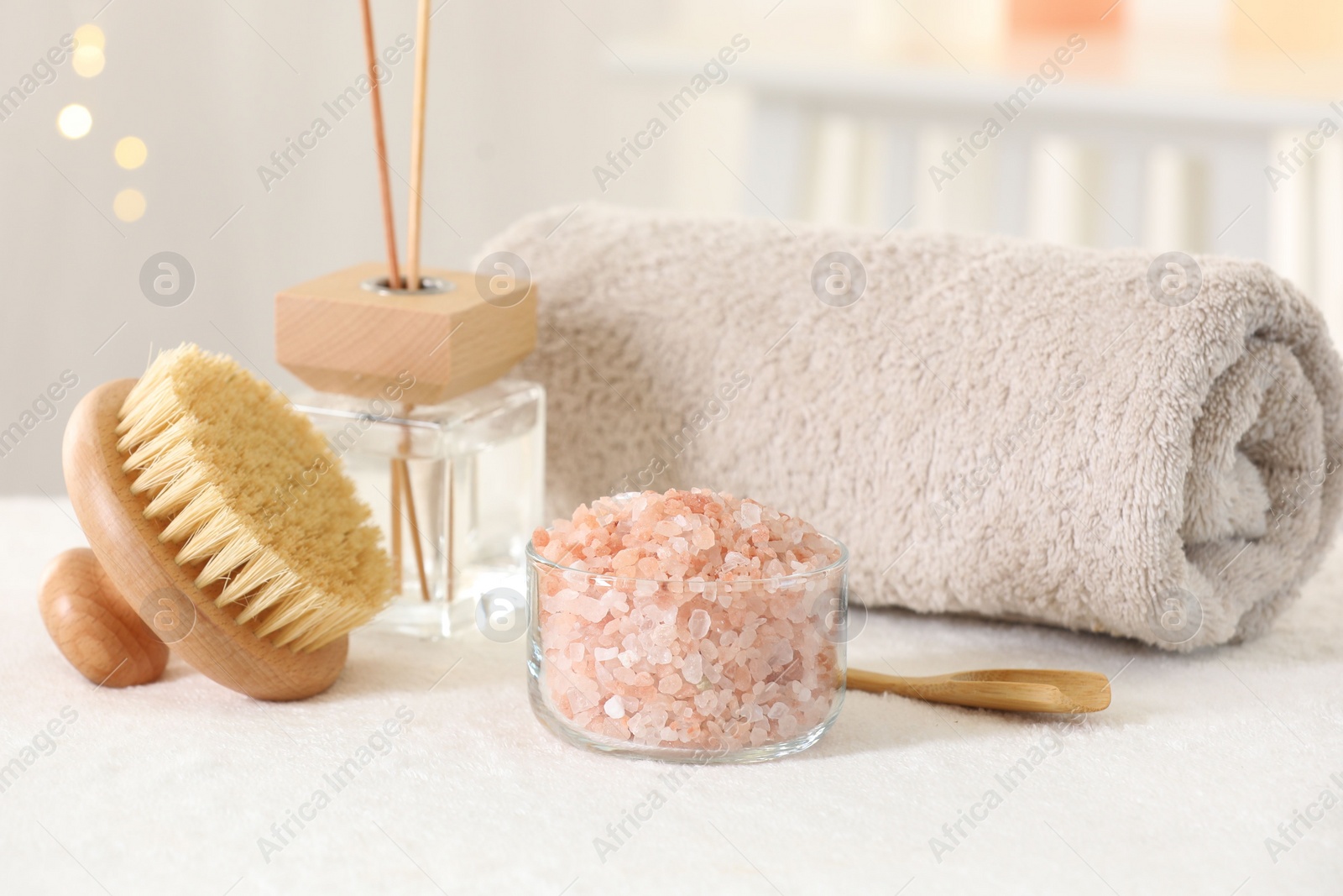 Photo of Spa composition. Sea salt, brush, towel and reed air freshener on soft white surface