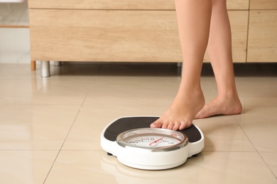 Photo of Woman stepping on floor scales in bathroom. Overweight problem