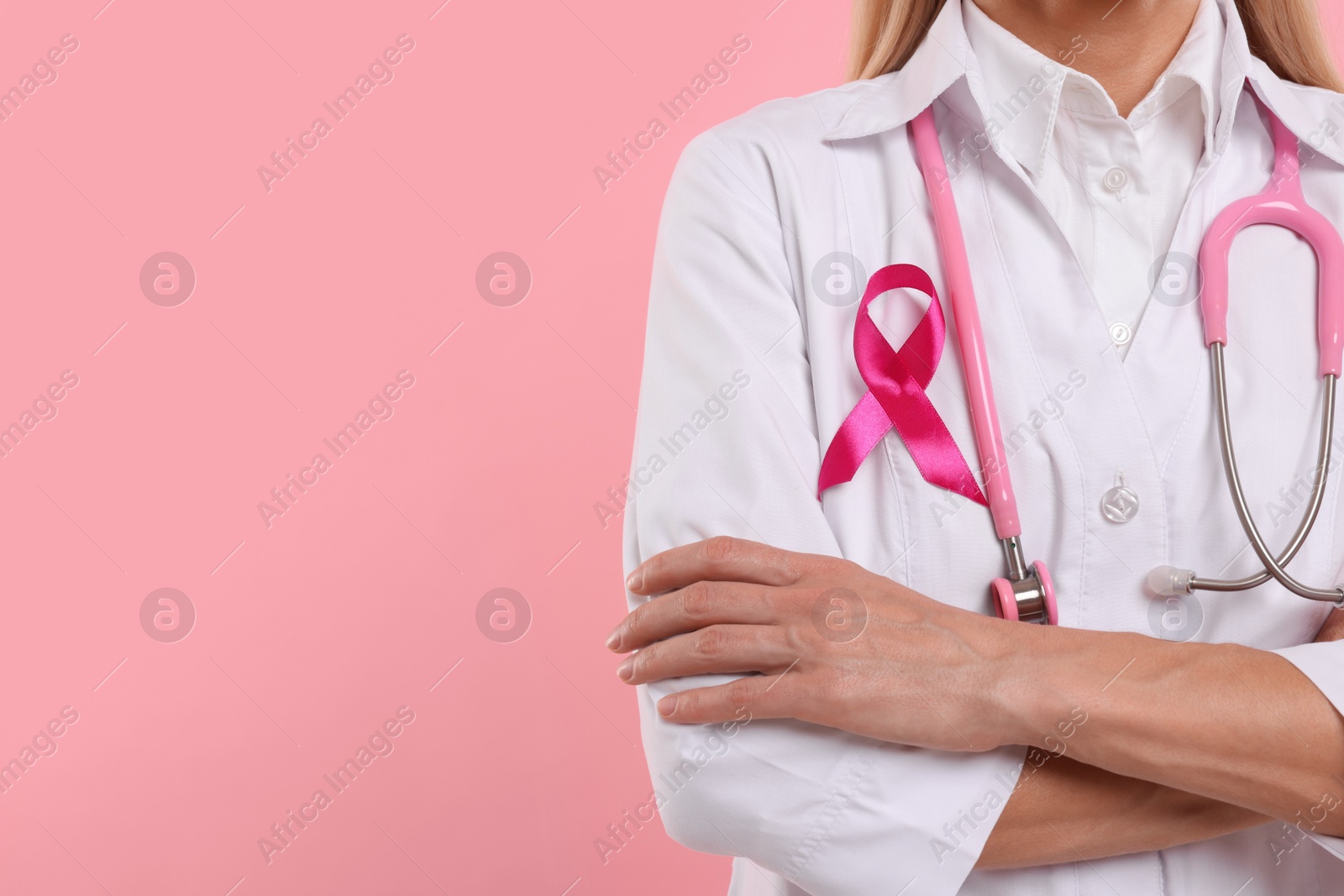 Photo of Doctor with pink ribbon and stethoscope on color background, closeup and space for text. Breast cancer awareness