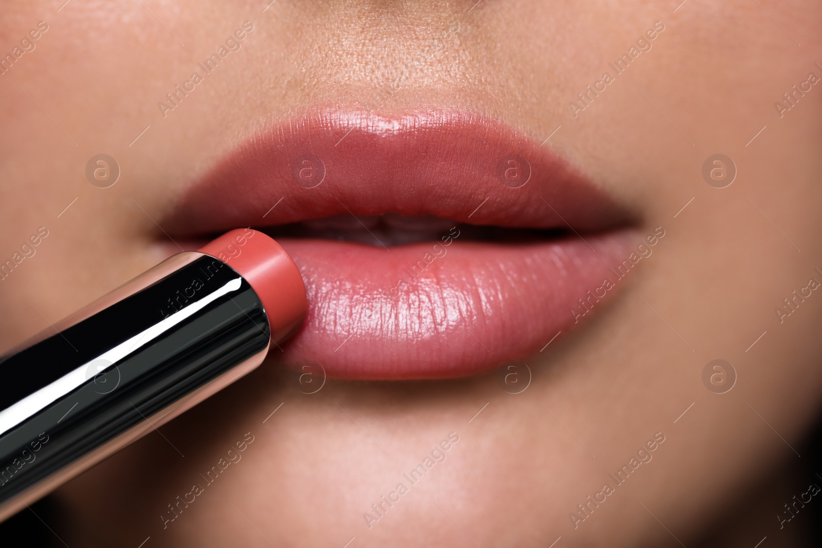 Photo of Closeup view of young woman applying beautiful nude lipstick