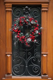 Photo of Beautiful Christmas wreath with berries and cones hanging on door