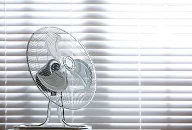 Modern electric fan on table near window indoors. Space for text