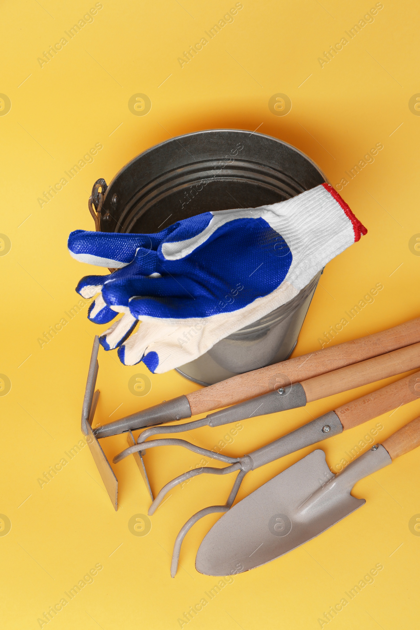 Photo of Bucket with gardening gloves and tools on yellow background, flat lay