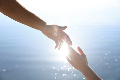 Photo of Man and woman reaching hands to each other over water, closeup. Nature healing power