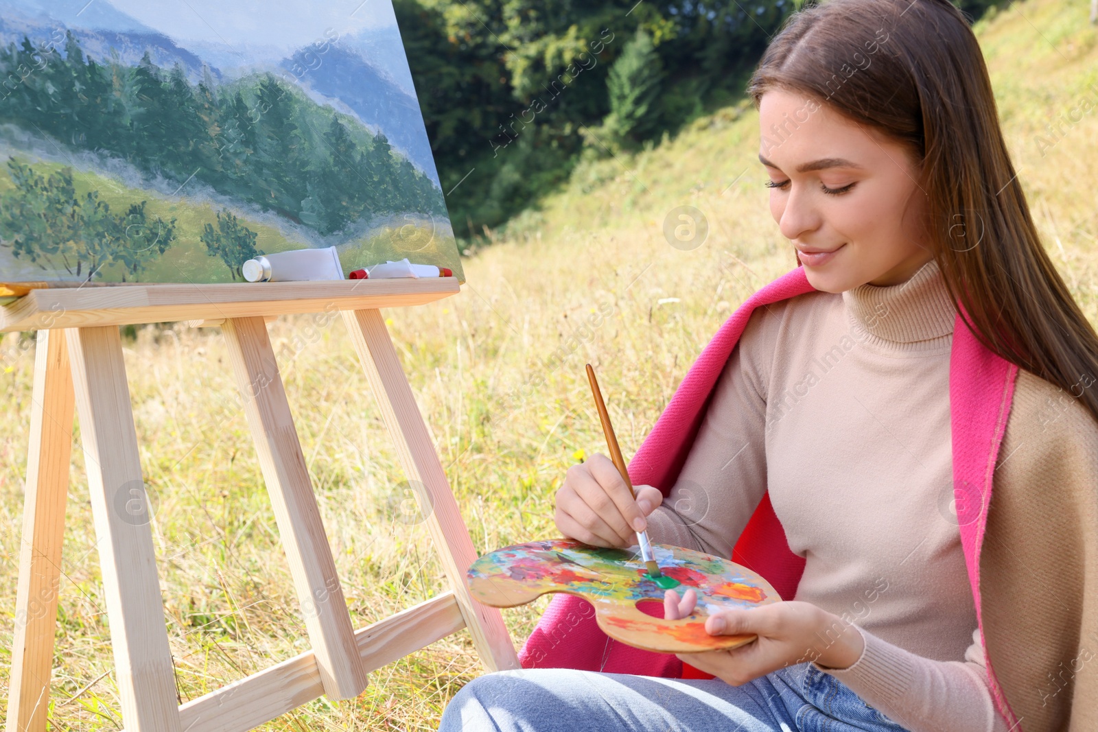 Photo of Young woman drawing on easel with brush outdoors