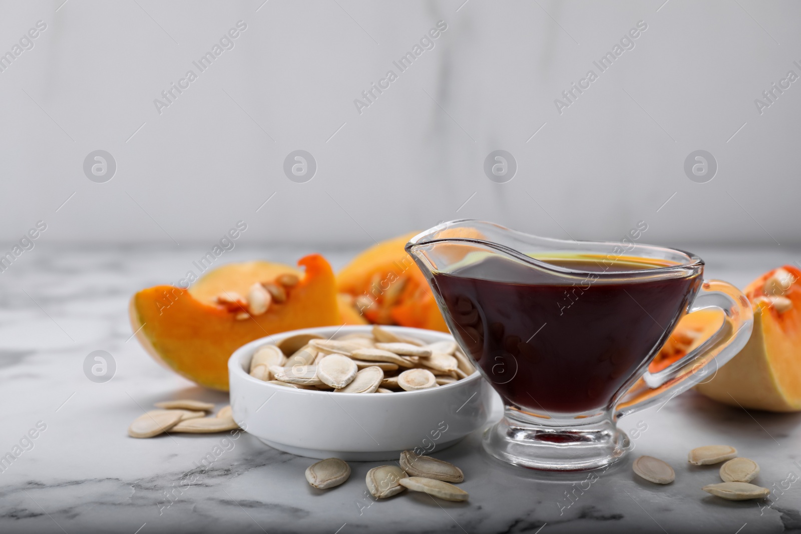 Photo of Fresh pumpkin seed oil in glass sauceboat on white marble table. Space for text