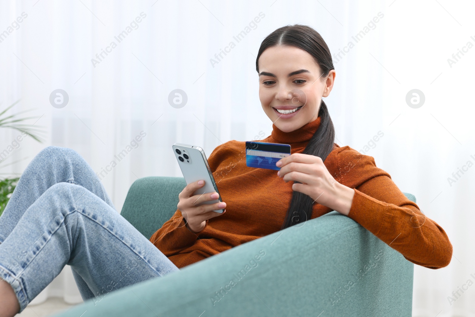 Photo of Happy young woman with smartphone and credit card shopping online on sofa at home