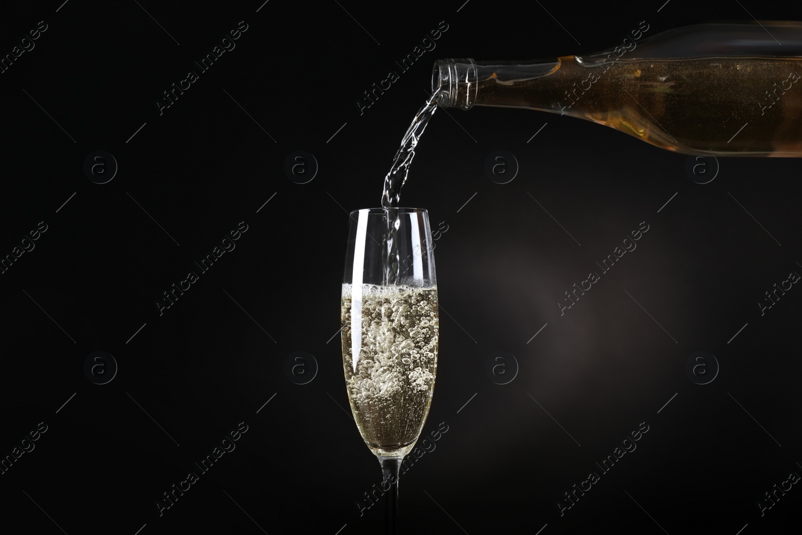 Photo of Pouring sparkling wine from bottle into glass on black background