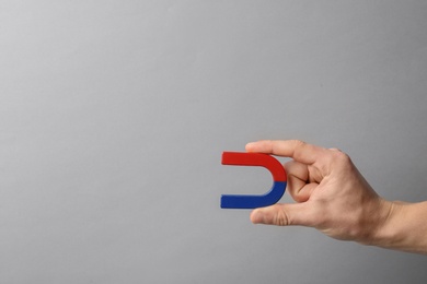 Man holding magnet on grey background, closeup. Space for text