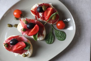 Photo of Delicious sandwiches with bresaola, cream cheese, olives and tomato on light table, top view