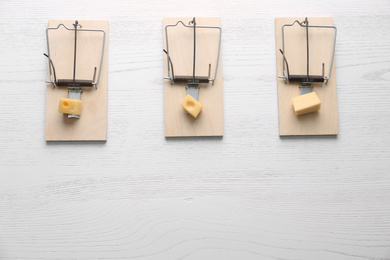 Photo of Mousetraps with pieces of cheese and space for text on white wooden background, flat lay. Pest control