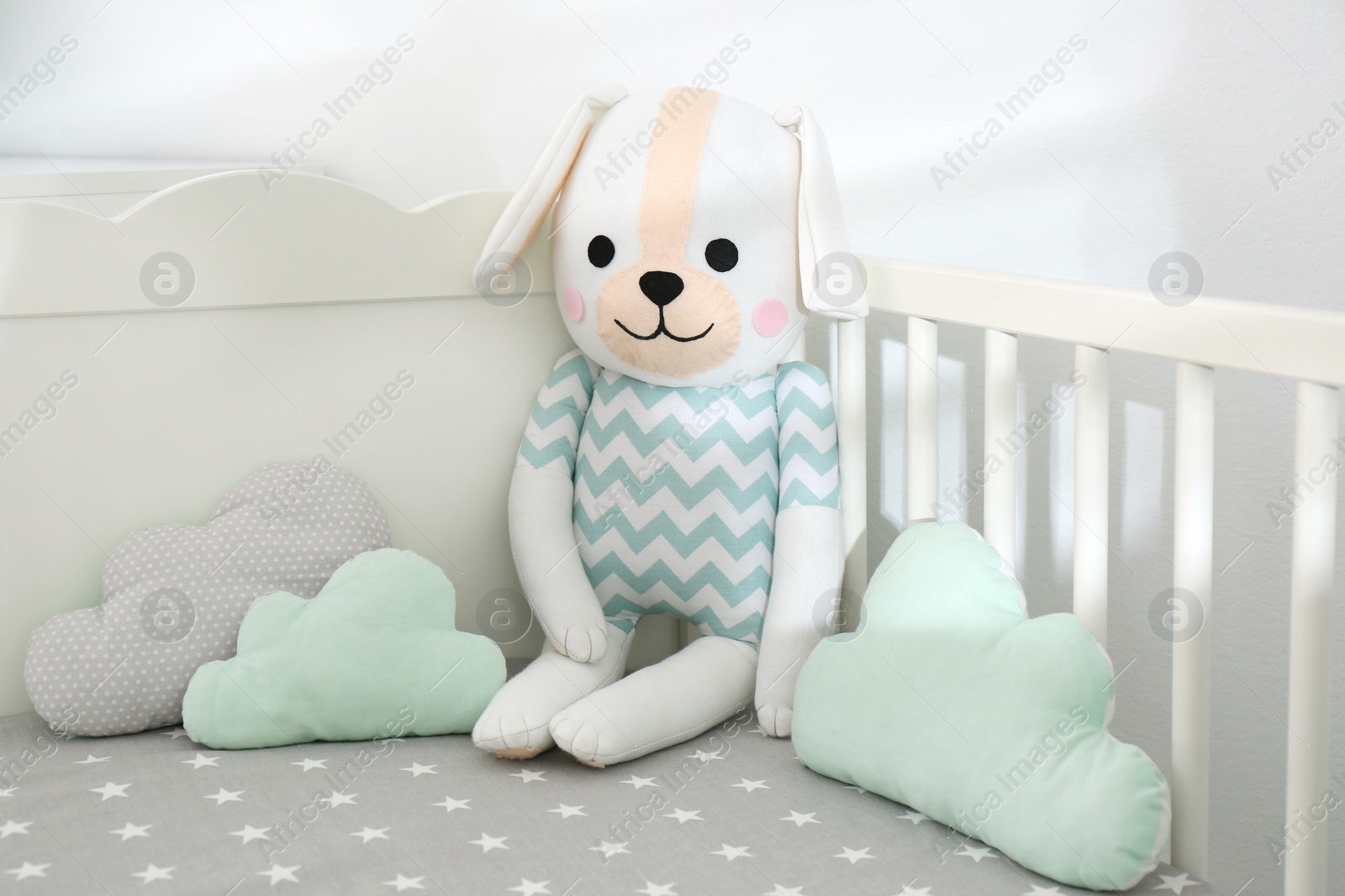 Photo of Cute toy dog and cloud shaped pillows in crib, closeup. Baby room interior elements