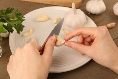 Photo of Woman peeling fresh garlic at table, closeup