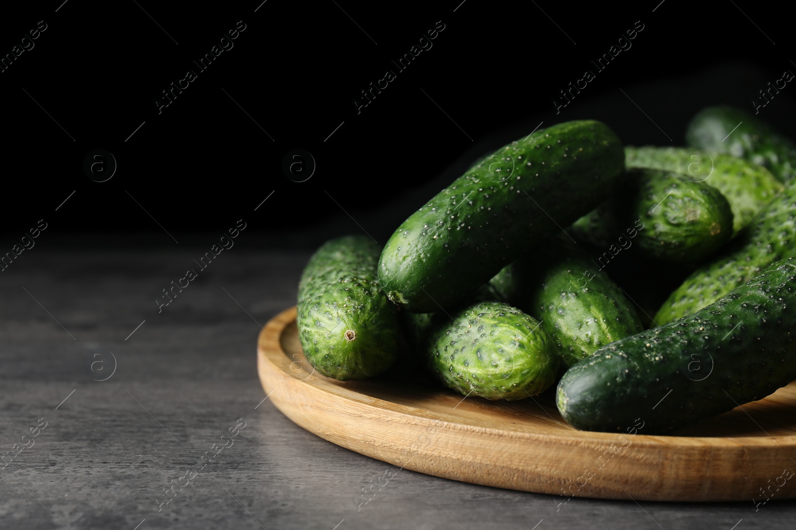 Photo of Wooden board with fresh ripe cucumbers on dark grey table, space for text