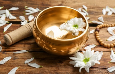 Photo of Golden singing bowl with flower and mallet on wooden table, closeup. Sound healing