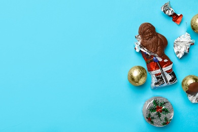 Chocolate Santa Claus and sweets on light blue background, flat lay. Space for text