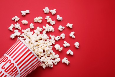 Photo of Overturned paper cup with delicious popcorn on red background, flat lay. Space for text