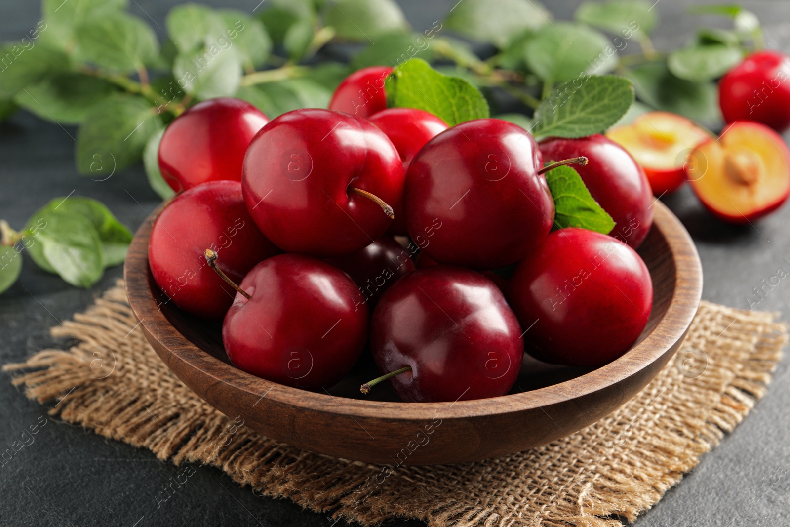 Photo of Delicious ripe cherry plums with leaves on black table