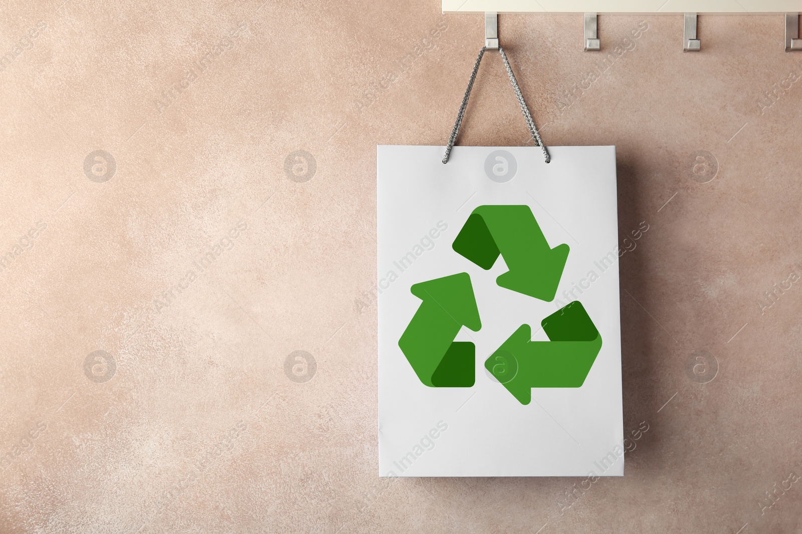 Image of Paper shopping bag with recycling symbol hanging on beige wall. Space for text