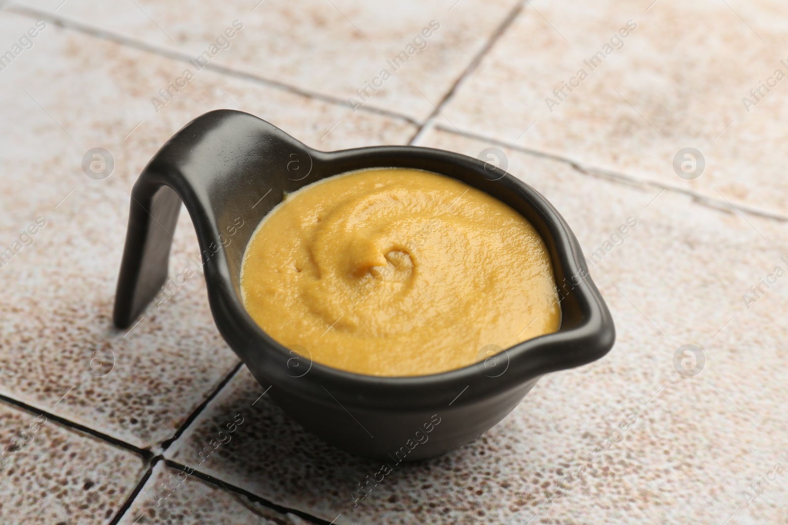 Photo of Tasty mustard sauce in saucepan on light tiled table, closeup