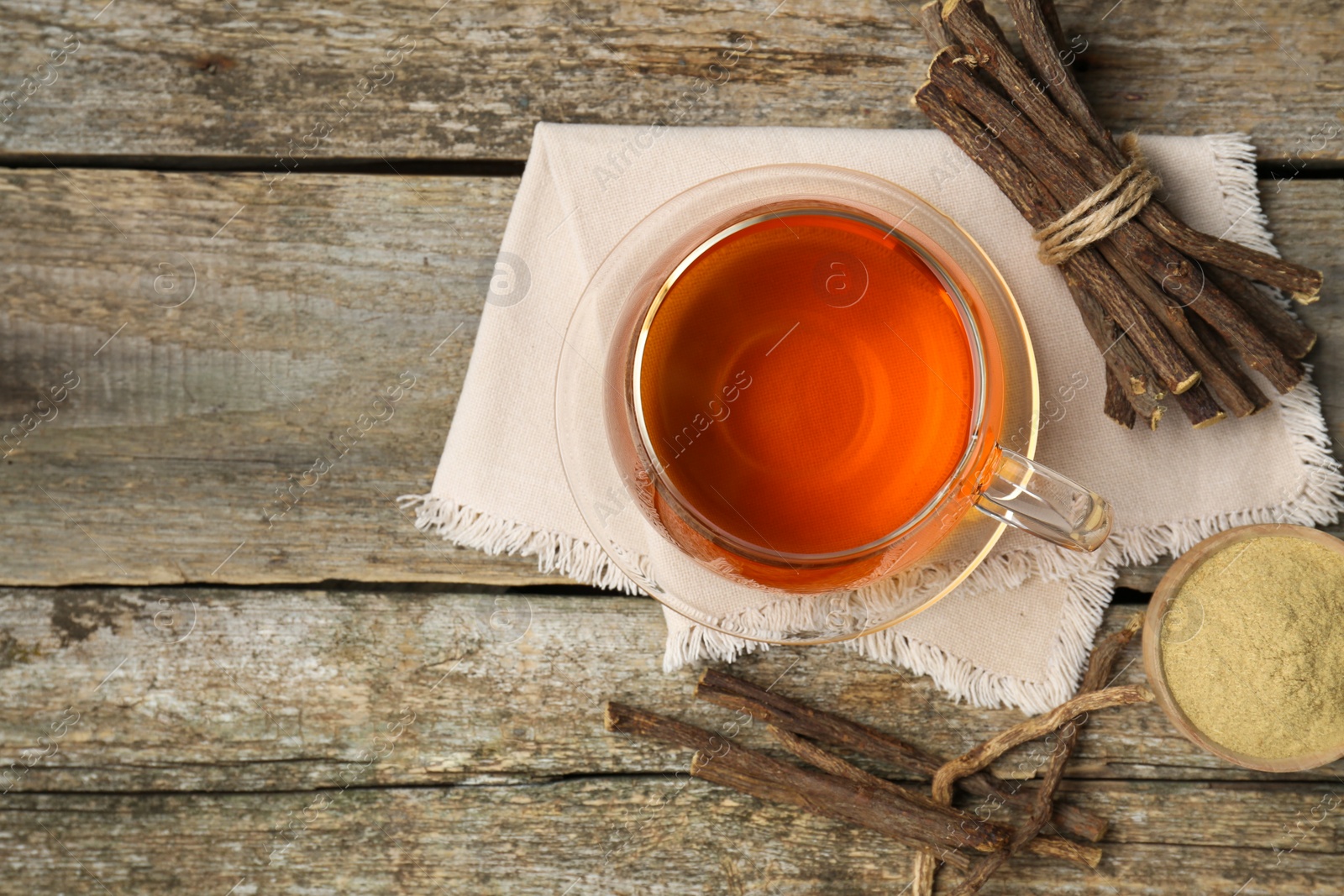 Photo of Aromatic licorice tea in cup, dried sticks of licorice root and powder on wooden table, flat lay. Space for text