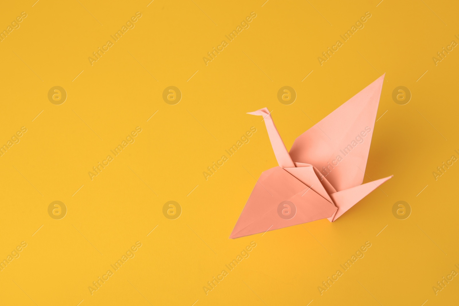 Photo of Origami art. Beautiful pale pink paper crane on orange background, space for text