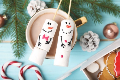 Flat lay composition with funny snowmen made of marshmallows in cup of hot drink on light blue wooden table